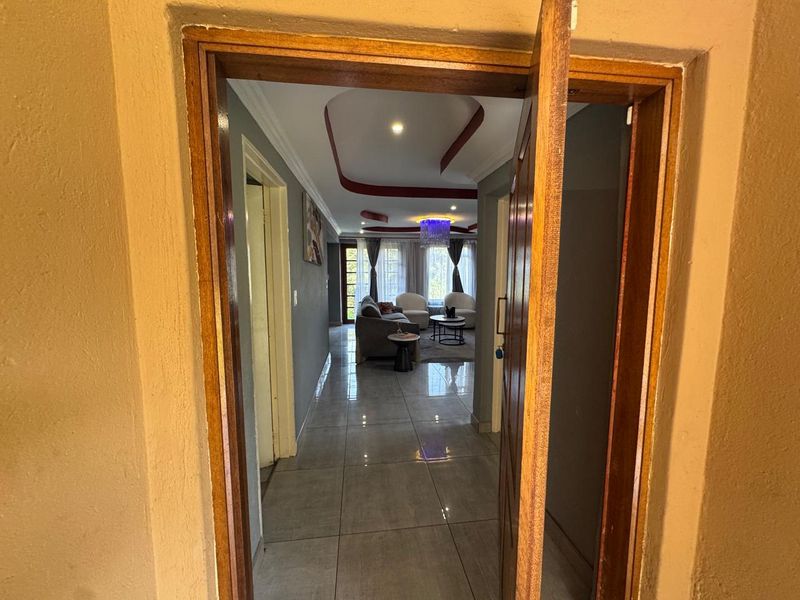 A view through a wooden doorway into a tiled hallway leading to an open-plan living area with a decorative recessed ceiling.