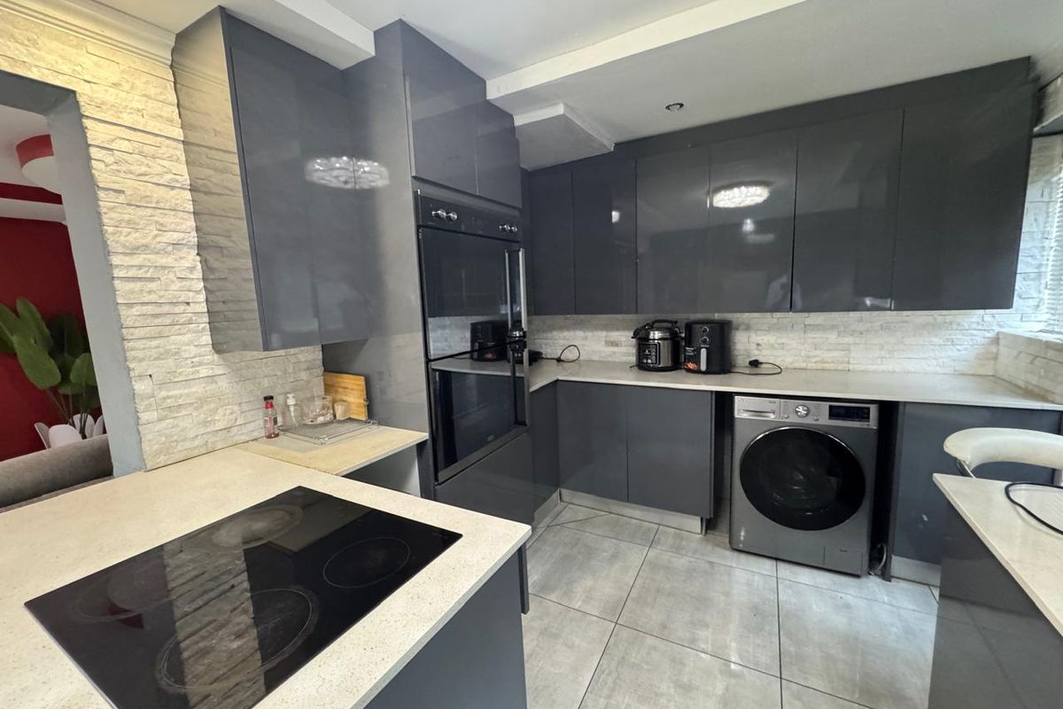 Modern kitchen featuring high-gloss grey cabinetry, stone countertops, built-in oven, electric hob, and stone-clad backsplash with tiled flooring.