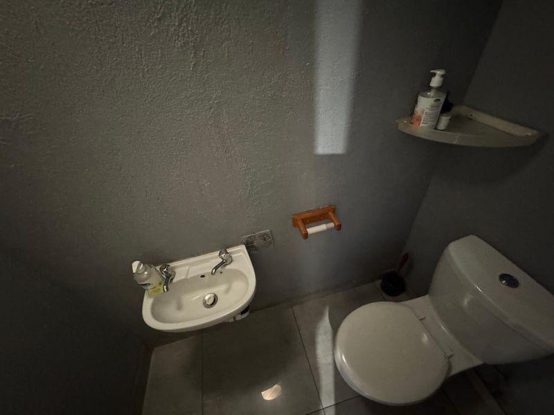 A compact bathroom featuring a wall-mounted basin, toilet, and tiled flooring, requiring cosmetic updates to improve the overall finish and lighting.