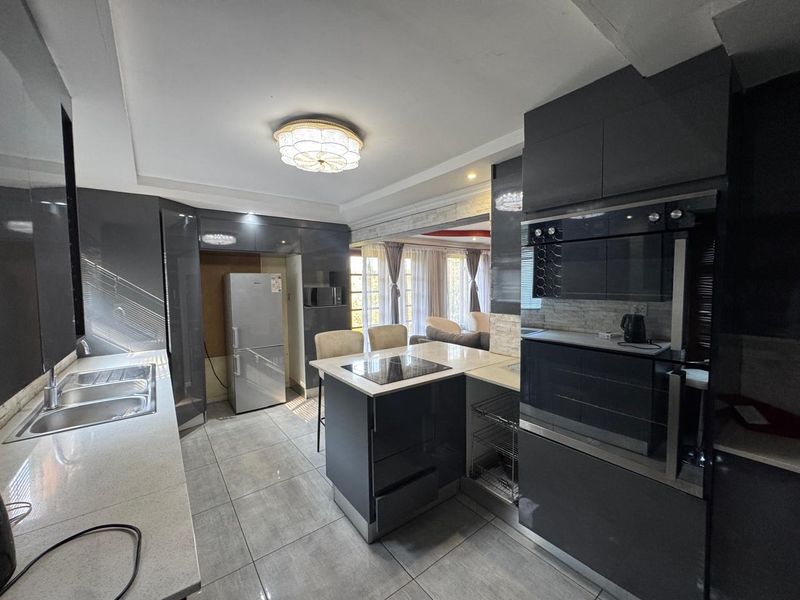 Modern kitchen featuring high-gloss cabinetry, stone countertops, integrated oven, electric hob, and tiled flooring, seamlessly flowing into the adjacent living area.