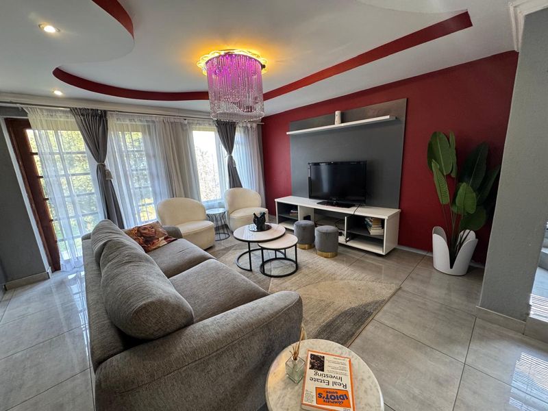 A modern living room featuring a bold red accent wall, a built-in media unit, tiled flooring, and a decorative recessed ceiling with feature lighting.