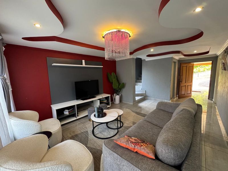 A contemporary living room featuring a decorative ceiling bulkhead with recessed lighting, tiled floors, and a built-in media wall unit.
