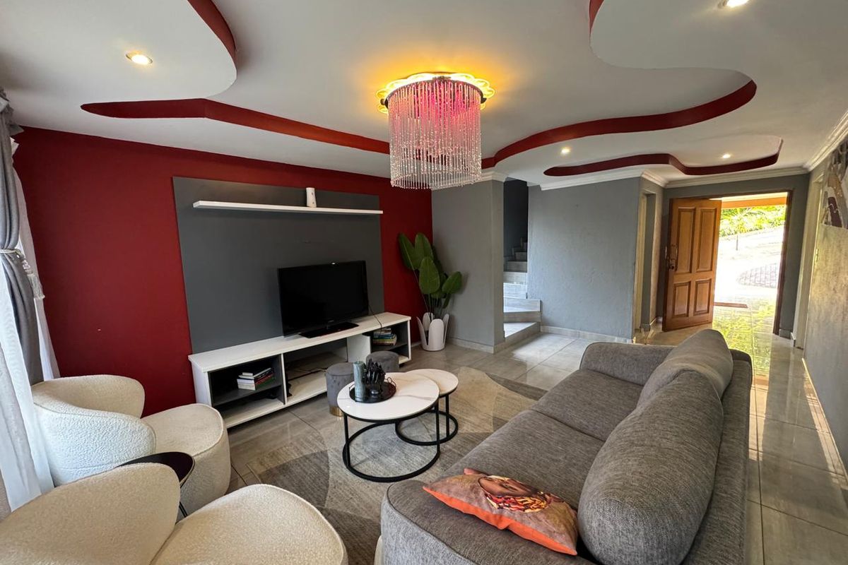 A contemporary living room featuring a decorative ceiling bulkhead with recessed lighting, tiled floors, and a built-in media wall unit.