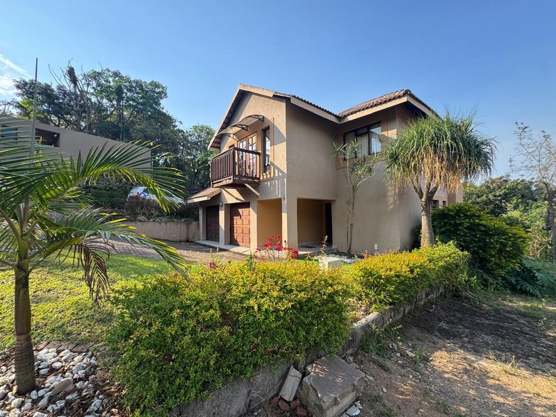 Front elevation of a double-story residential house featuring a balcony, double garage, and paved driveway set within a landscaped garden.