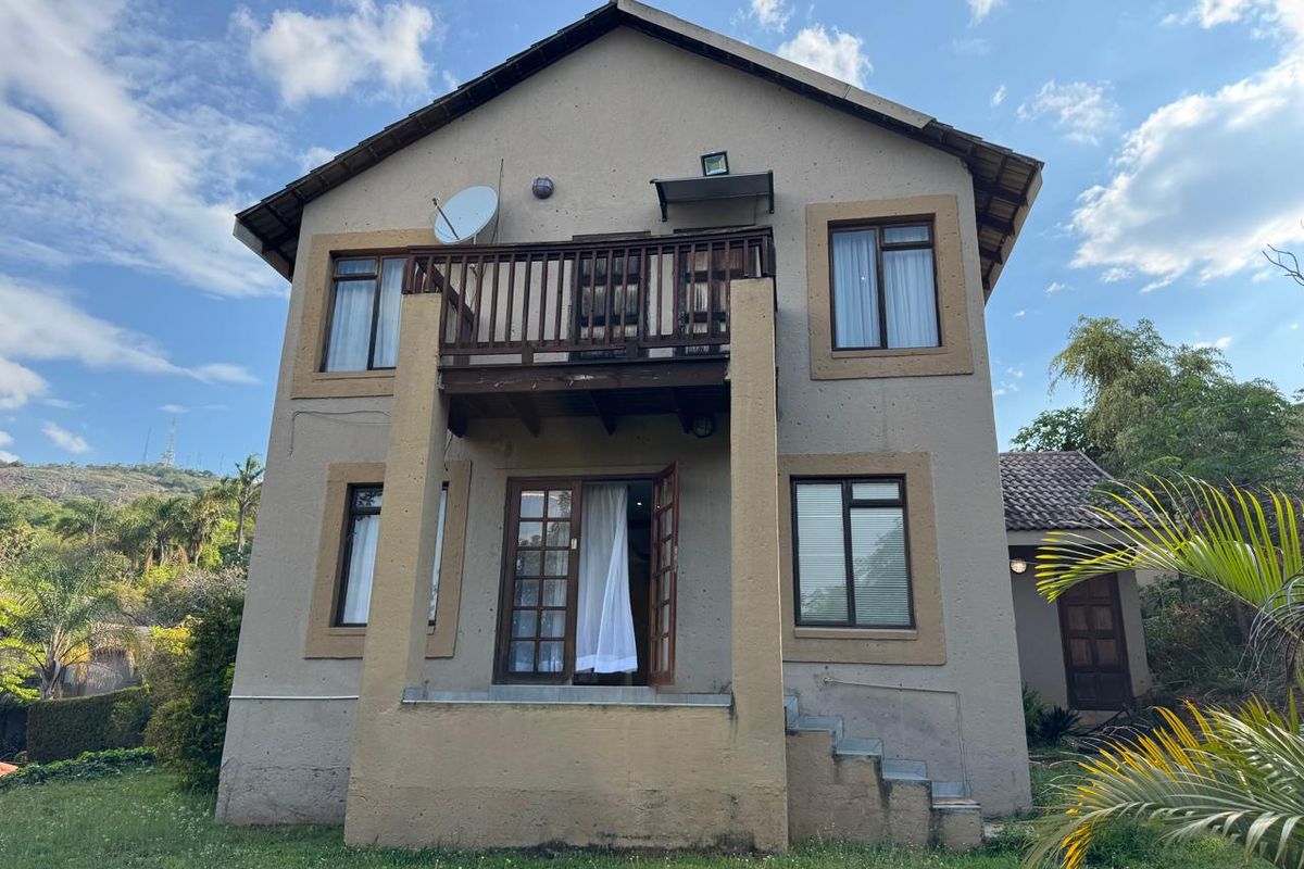 Rear view of a two-story house featuring a balcony with wooden balustrade, french doors, and a garden area.
