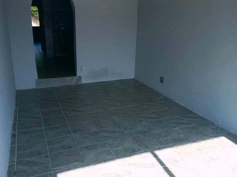 An empty living room featuring grey tiled flooring, a ceiling fan, and an arched doorway leading to an adjacent space.
