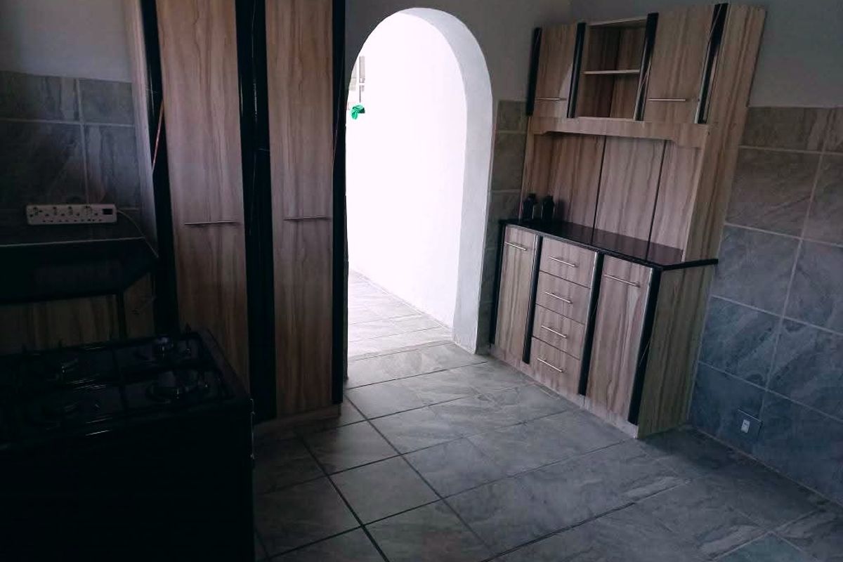 A functional kitchen area featuring built-in wooden cabinetry, tiled flooring, and a distinctive arched doorway leading to an adjacent space.