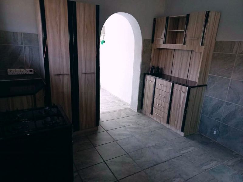 A functional kitchen area featuring built-in wooden cabinetry, tiled flooring, and a distinctive arched doorway leading to an adjacent space.