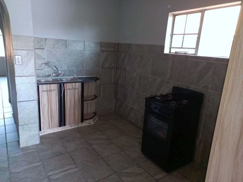 A functional kitchen area featuring tiled walls and flooring, a single sink unit with built-in cabinetry, and a freestanding stove.