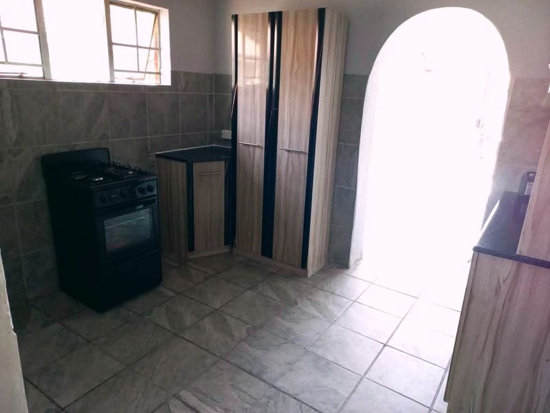 A functional kitchen featuring tiled flooring, tiled splashbacks, built-in cabinetry, and a gas stove, with an arched doorway leading to an adjacent space.
