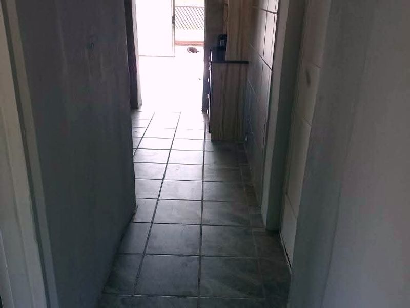A narrow hallway featuring tiled flooring and an arched entryway leading to an exterior space, with built-in cabinetry visible along the side wall.