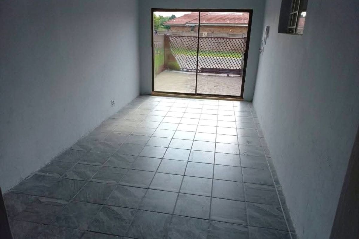 An empty, tiled living area featuring a sliding glass door that provides access to the exterior.