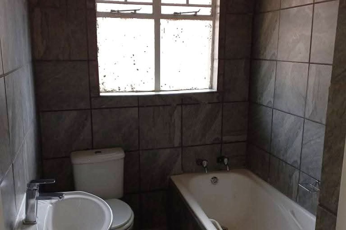 A functional bathroom featuring a pedestal basin, toilet, and bathtub with full-height wall tiling and floor tiles.