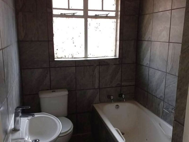 A functional bathroom featuring a pedestal basin, toilet, and bathtub with full-height wall tiling and floor tiles.