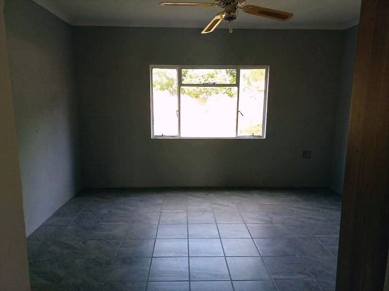 An empty bedroom featuring tiled flooring, a ceiling fan, and a large window providing natural light.