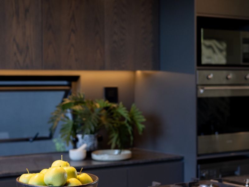 Modern kitchen featuring dark wood cabinetry, stone countertops, integrated appliances, and sleek pendant lighting, creating a sophisticated and functional culinary space.