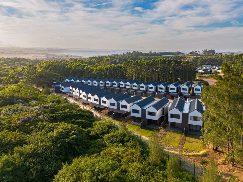 An aerial view of a modern townhouse development complex surrounded by lush greenery and natural landscape.