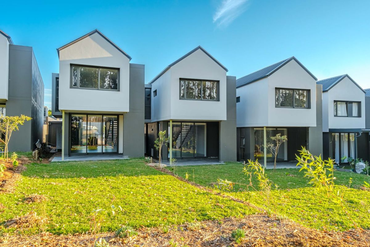 Rear view of modern townhouse complex featuring contemporary architectural design, sliding glass doors, and private patio areas overlooking a shared lawn.