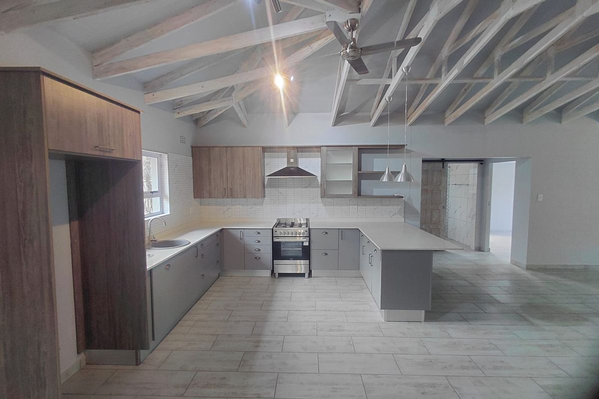 Modern kitchen featuring exposed timber rafters, sleek cabinetry, stainless steel gas stove, and tiled flooring in an open-plan layout.