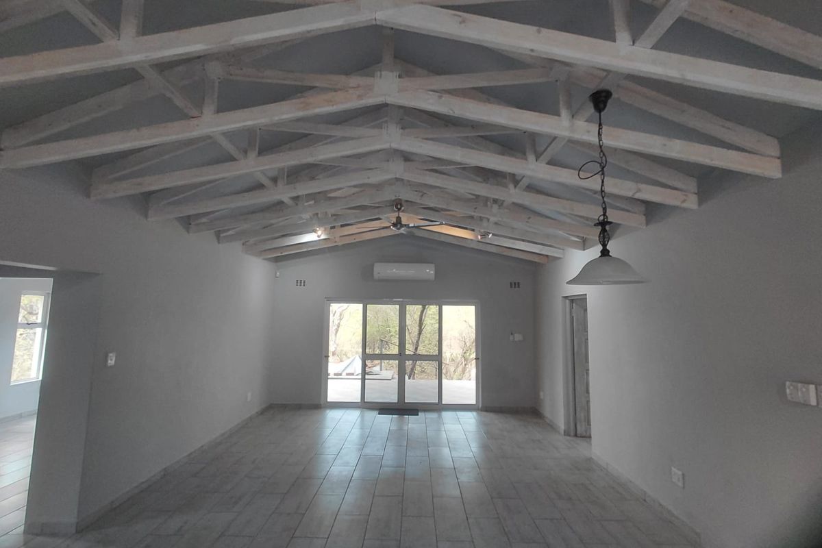 Spacious open-plan living area featuring high vaulted ceilings with exposed timber trusses, tiled flooring, and large sliding doors leading to the outdoors.