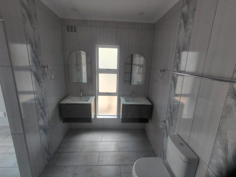 Modern bathroom featuring a double vanity with wall-mounted basins, neutral floor-to-ceiling tiling, and a clean, contemporary layout.