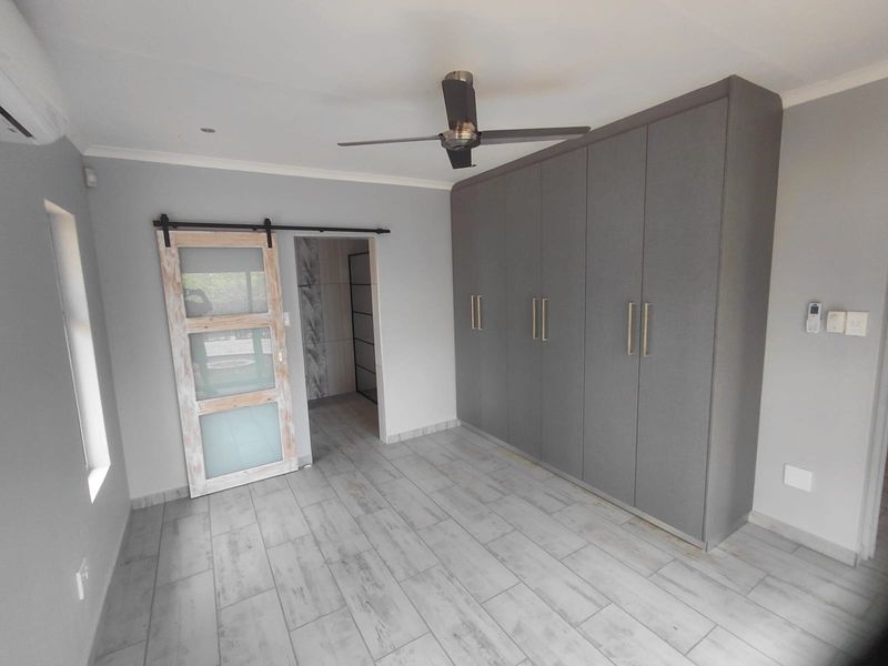 A modern, empty bedroom featuring grey built-in cupboards, a sliding barn door, tiled flooring, and a ceiling fan.