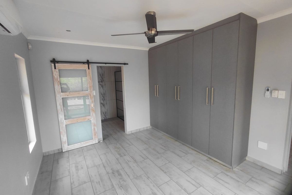 A modern, empty bedroom featuring grey built-in cupboards, a sliding barn door, tiled flooring, and a ceiling fan.