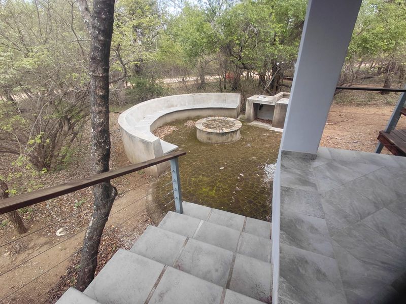 Outdoor patio area featuring a built-in concrete fire pit, curved bench seating, and a prep station, accessible via a tiled staircase.
