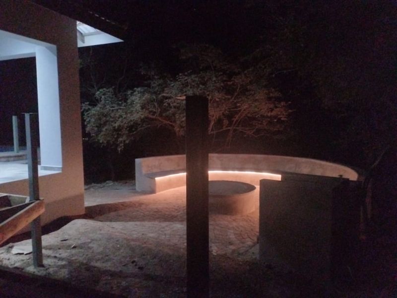 Outdoor patio area at night featuring a built-in curved concrete bench with integrated LED lighting and paved flooring.