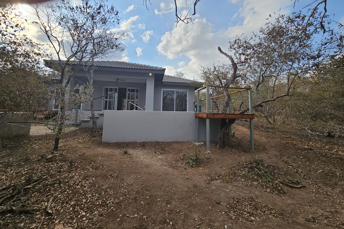 Rear view of the house featuring a raised wooden deck, concrete patio area, and sliding glass doors leading into the main living space.