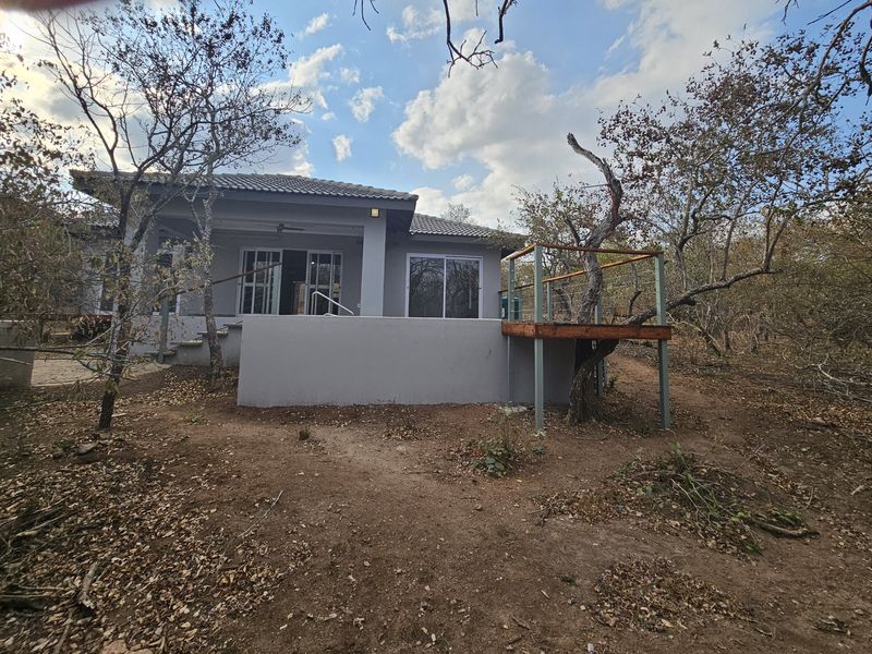 Rear view of the house featuring a raised wooden deck, concrete patio area, and sliding glass doors leading into the main living space.