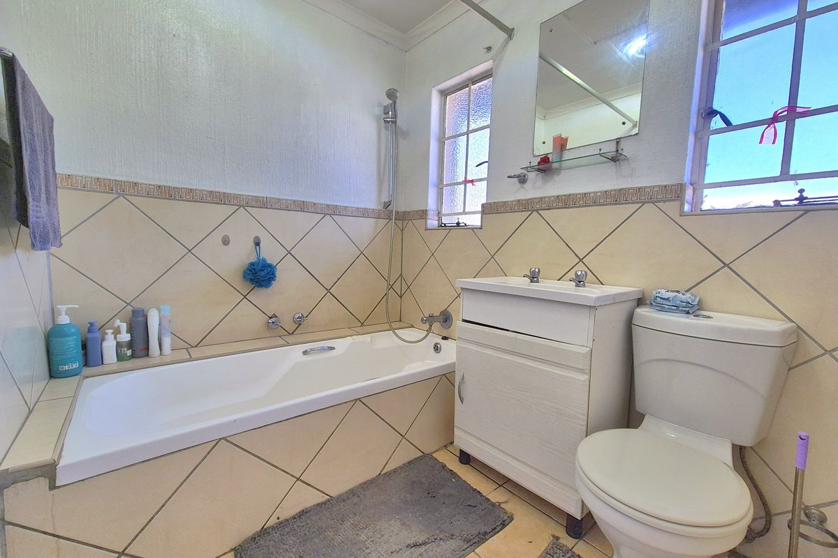 A functional bathroom featuring a built-in bathtub, vanity cabinet, and standard toilet, finished with neutral ceramic wall and floor tiles.