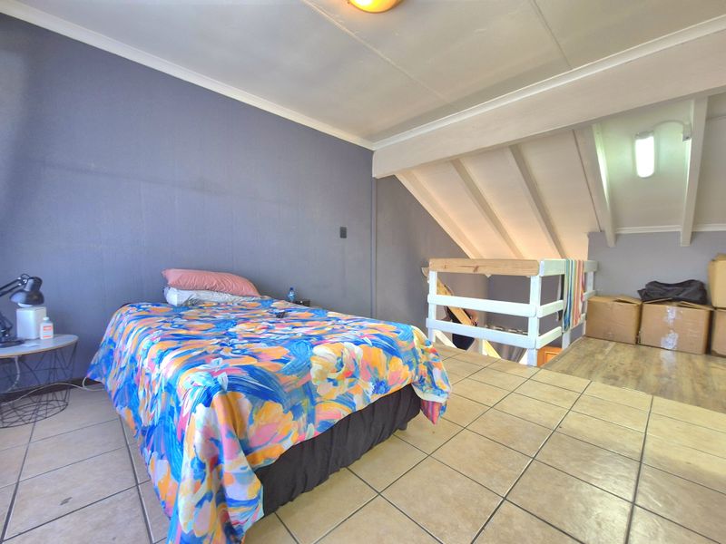 A loft-style bedroom featuring tiled flooring, exposed timber rafters, and a mezzanine level with a timber balustrade.