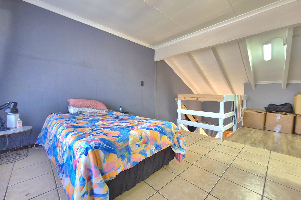 A loft-style bedroom featuring tiled flooring, exposed timber rafters, and a mezzanine level with a timber balustrade.