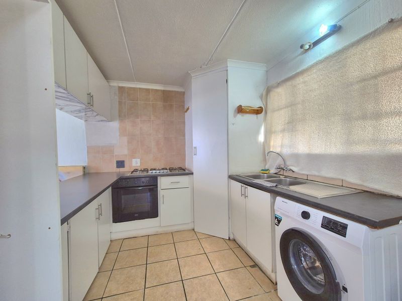 Functional kitchen featuring built-in cabinetry, gas hob, oven, double sink, and tiled flooring, offering a practical layout with ample storage space.