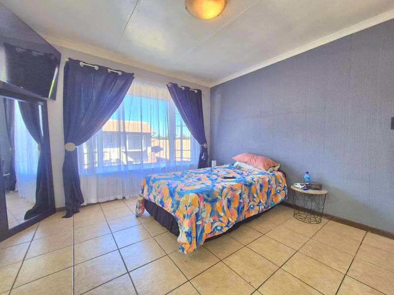 A bedroom featuring tiled flooring, a large window allowing natural light, and a neutral wall finish.