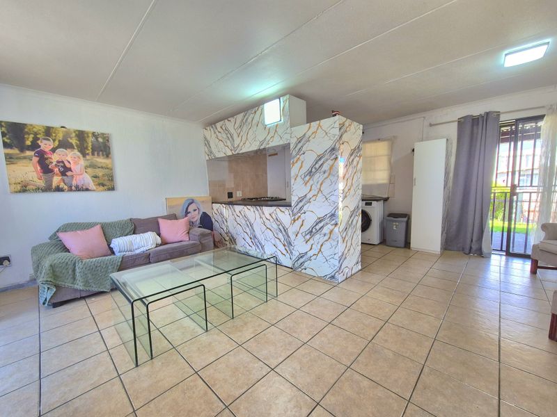 Open-plan living area featuring tiled flooring, a marble-effect kitchen island with built-in hob, and direct access to an outdoor patio area.