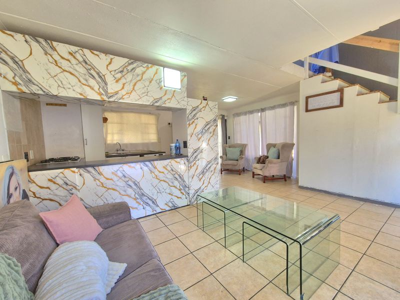 Open-plan living and kitchen area featuring marble-effect cabinetry, tiled flooring, and a staircase leading to the upper level.