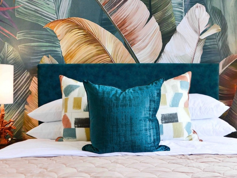 A well-appointed bedroom featuring a bold tropical-themed feature wall and a plush upholstered headboard, creating a stylish and comfortable sleeping space.