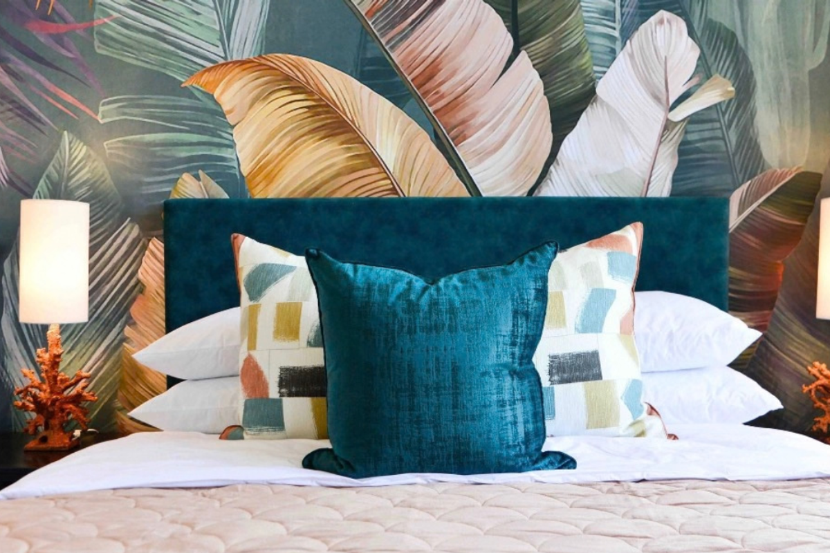 A well-appointed bedroom featuring a bold tropical-themed feature wall and a plush upholstered headboard, creating a stylish and comfortable sleeping space.