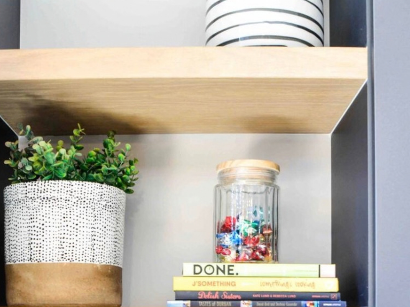 A close-up view of a modern built-in shelving unit with a light wood finish and dark grey surround.