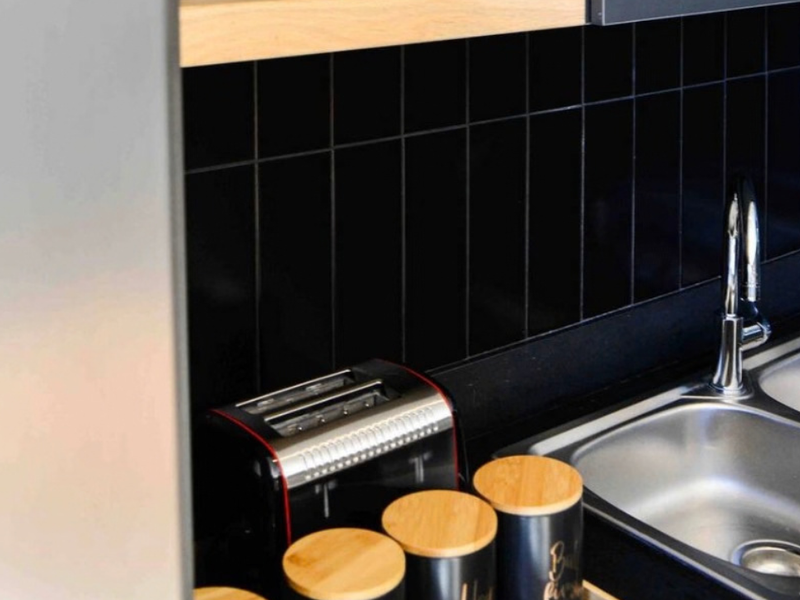 A modern kitchen area featuring a stainless steel double sink, chrome mixer tap, and a sleek black subway tile backsplash.