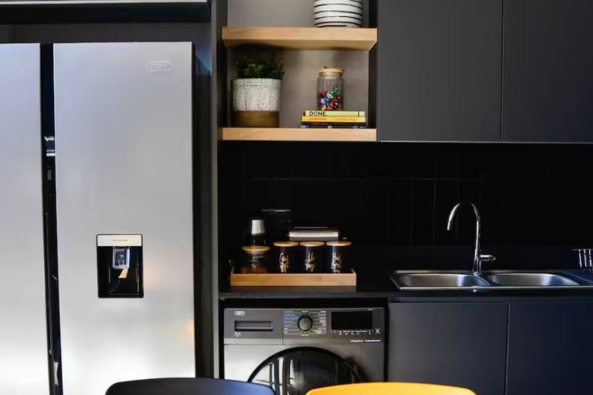 Modern kitchen featuring sleek dark cabinetry, integrated washing machine, double sink with mixer tap, and stylish open shelving with tiled splashback.