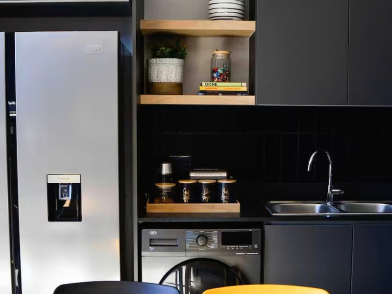 Modern kitchen featuring sleek dark cabinetry, integrated washing machine, double sink with mixer tap, and stylish open shelving with tiled splashback.