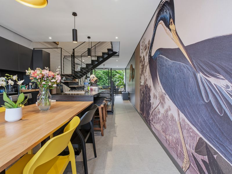 Modern open-plan living area featuring a sleek kitchen with island, tiled flooring, and a striking feature wall, complemented by a contemporary staircase.