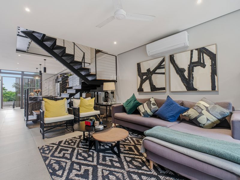Modern open-plan living area featuring a sleek staircase, tiled flooring, split-system air conditioning, and recessed lighting with access to an outdoor balcony.