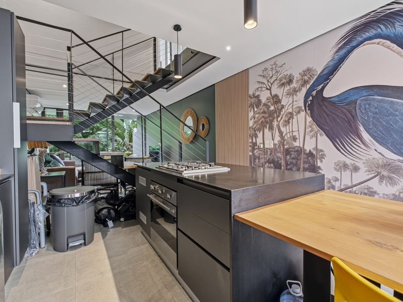Modern open-plan kitchen featuring sleek dark cabinetry, stone countertops, integrated gas hob and oven, adjacent to a contemporary staircase with metal balustrades.