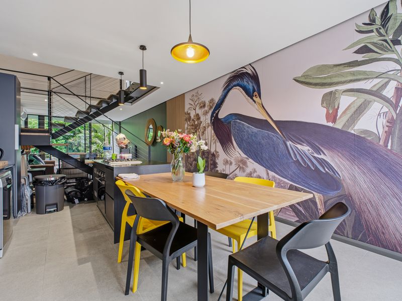Modern open-plan living and dining area featuring a sleek kitchen, contemporary metal staircase, and a striking feature wall with mural.