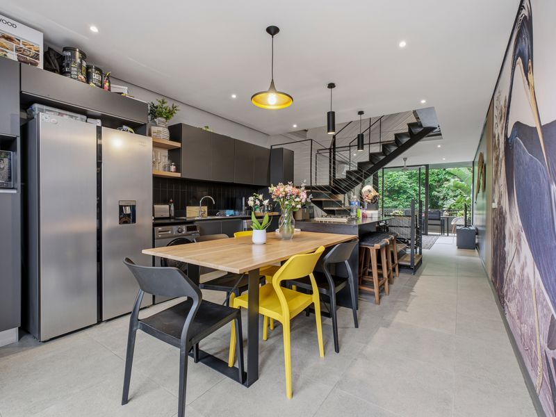 Modern open-plan kitchen and dining area featuring sleek cabinetry, tiled flooring, and a striking staircase leading to the upper level.
