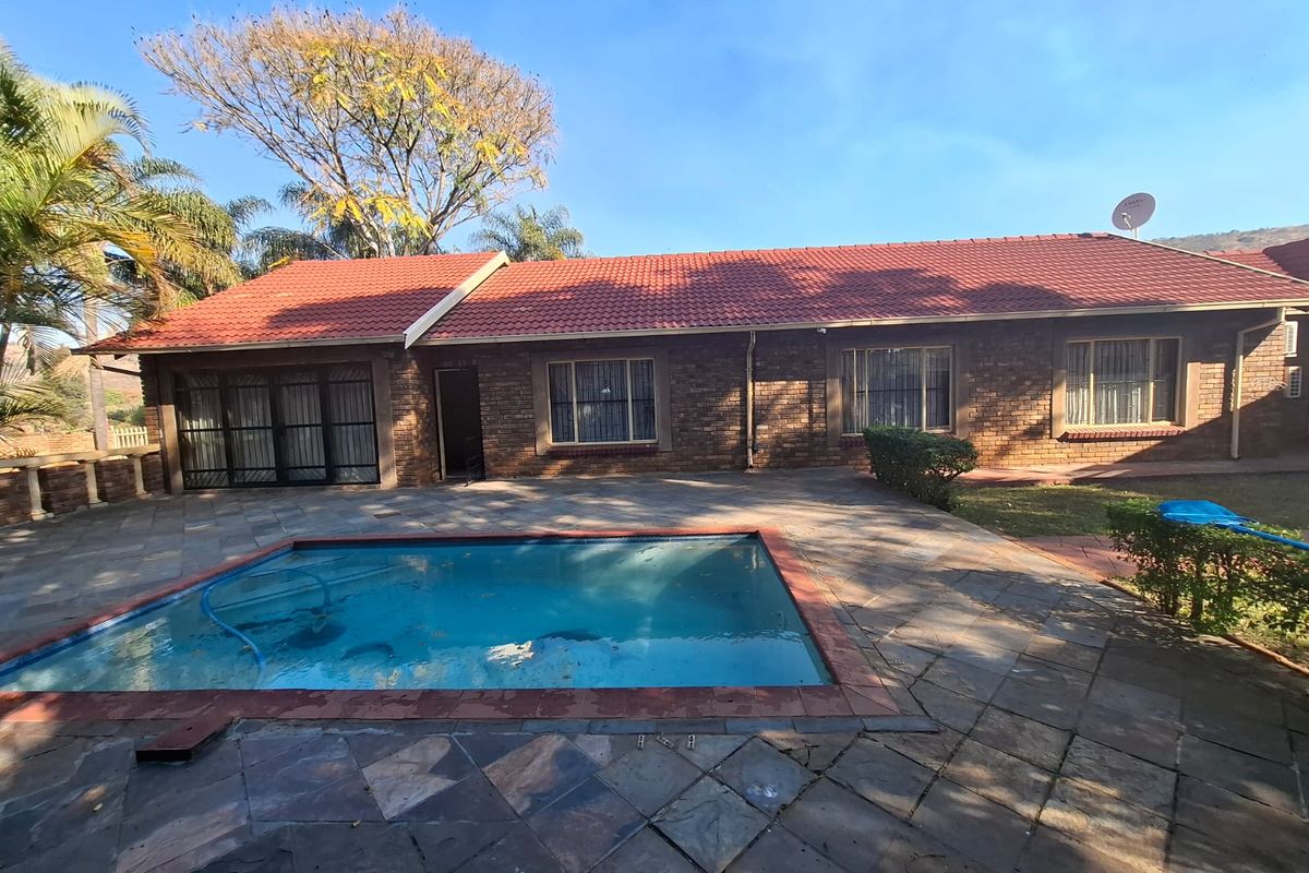 Rear exterior view of a brick house featuring a swimming pool and a paved patio area under a tiled roof.